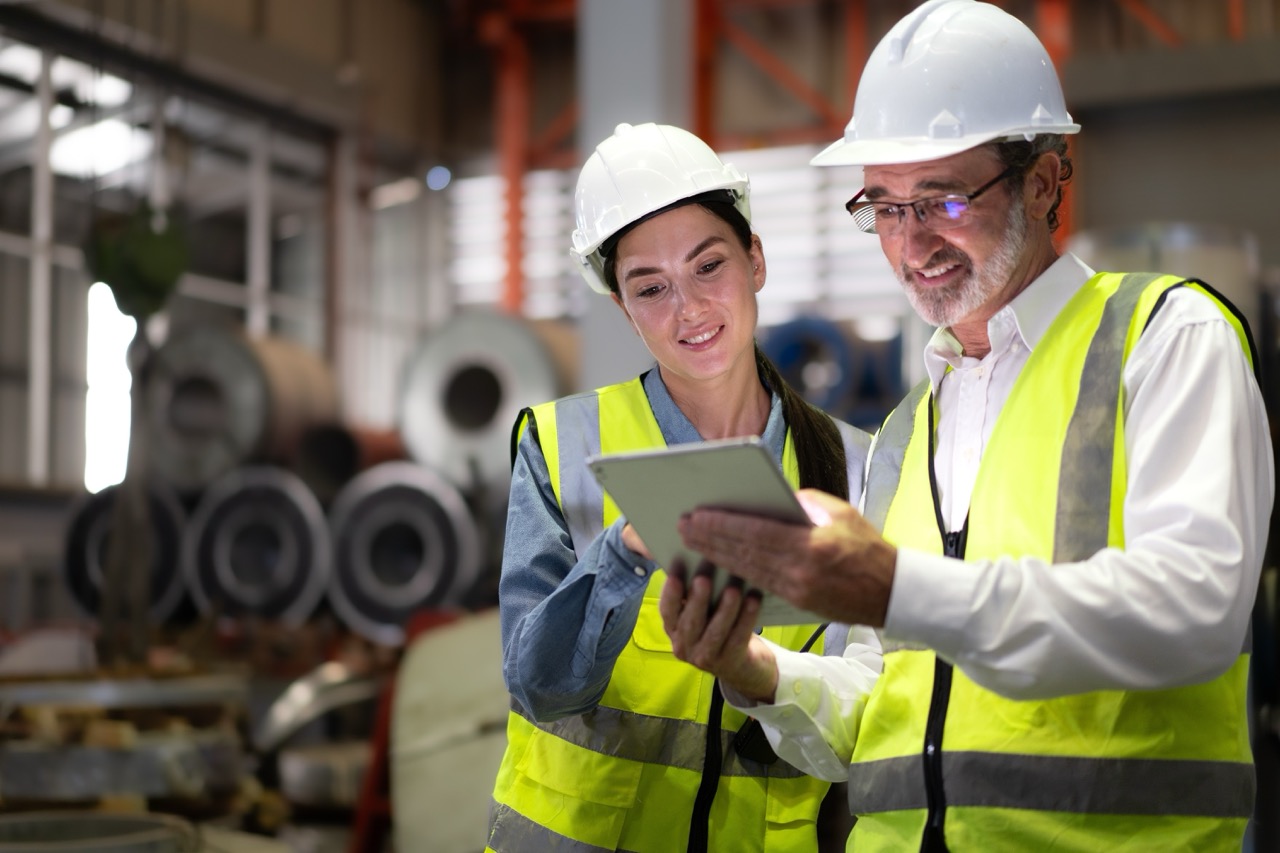 Smiling project managers in safety gear reviewing reduced operations costs achieved with efficient torque tools.