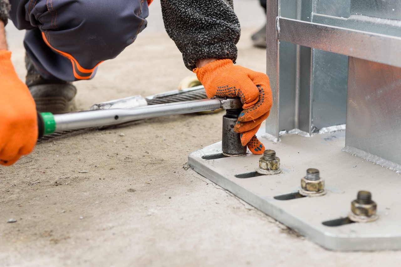 Construction worker uses torque wrench to tighten fasteners attaching machinery to ground.